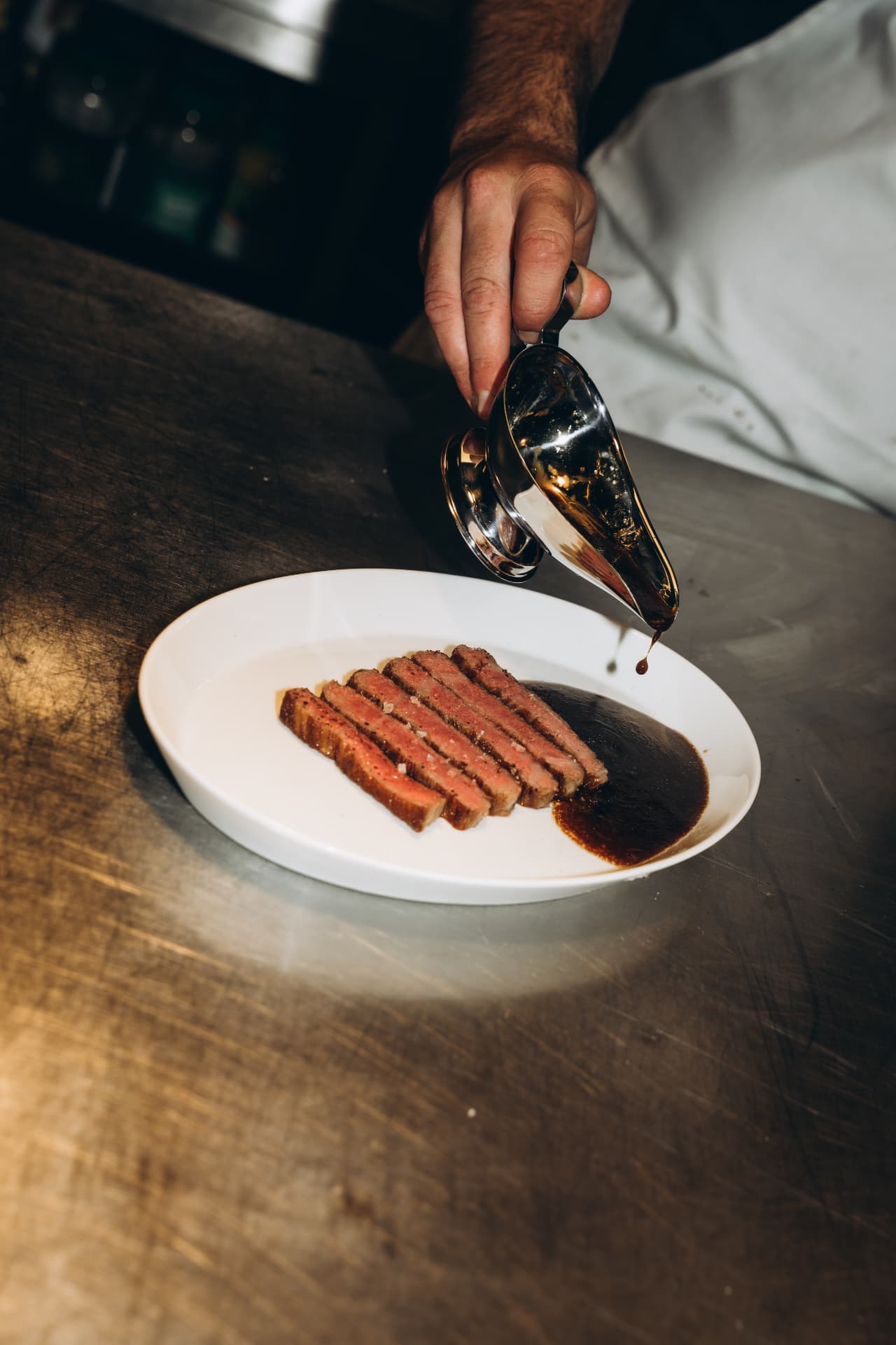 Sliced wagyu steak with beef jus being poured at the pass