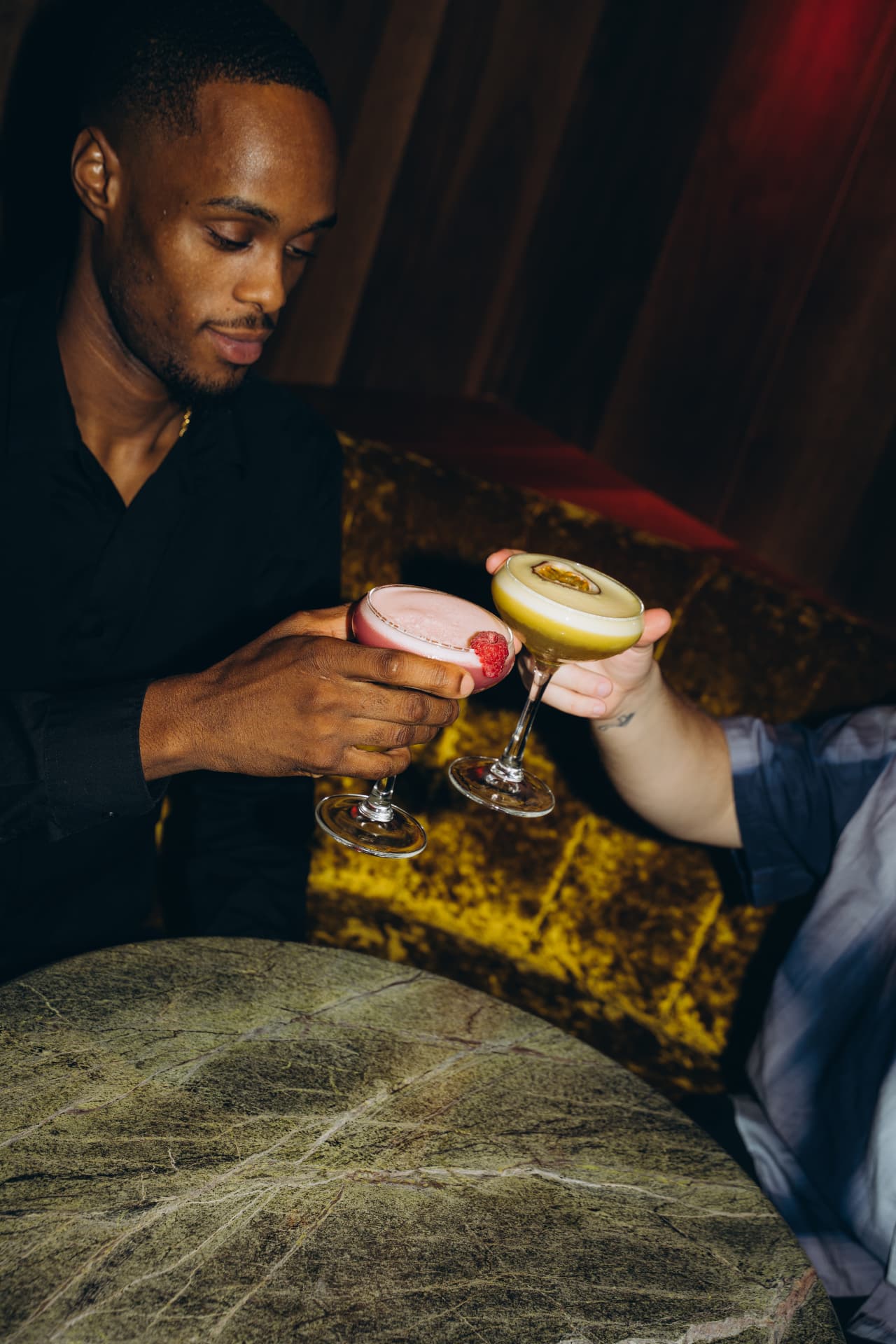 Two guests toasting with cocktails in a velvet booth