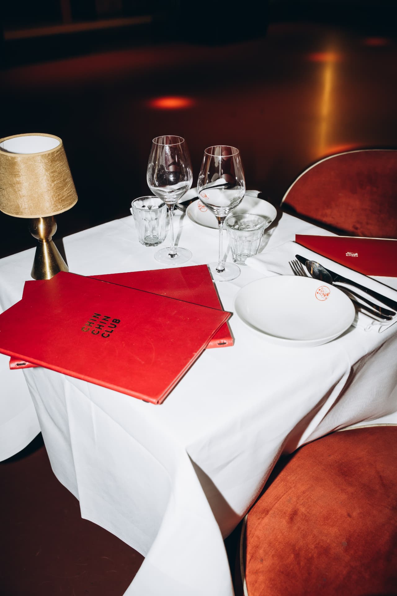 Table set at Le Souterrain with white linen, a red menu card and a brass lamp